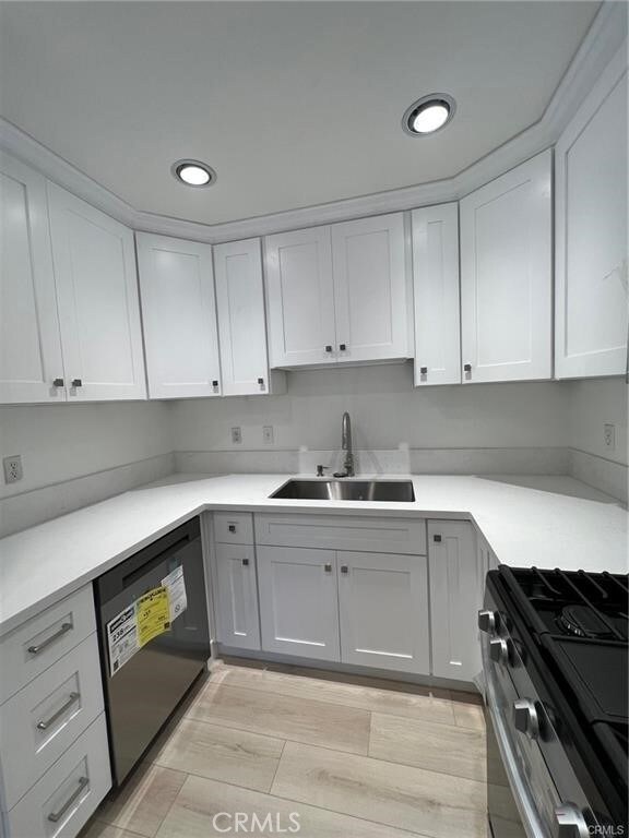 kitchen with sink, white cabinetry, black dishwasher, and stainless steel stove