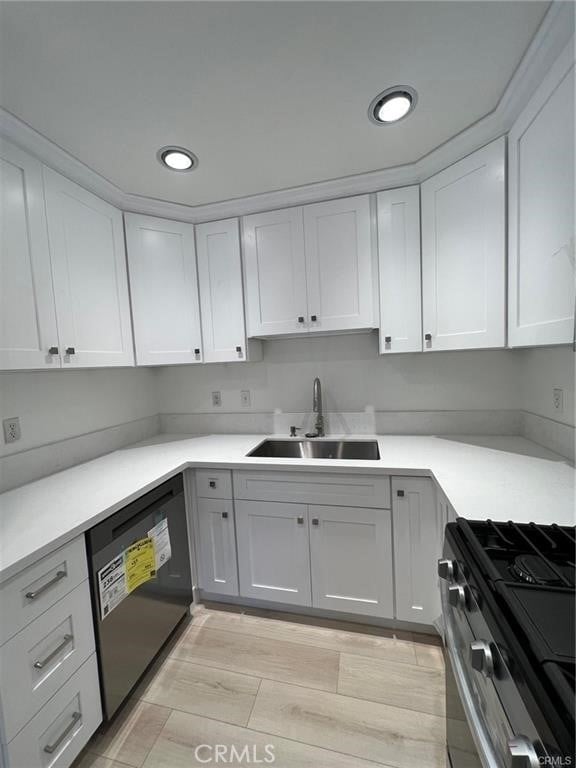 kitchen with black dishwasher, sink, white cabinets, stove, and light hardwood / wood-style floors