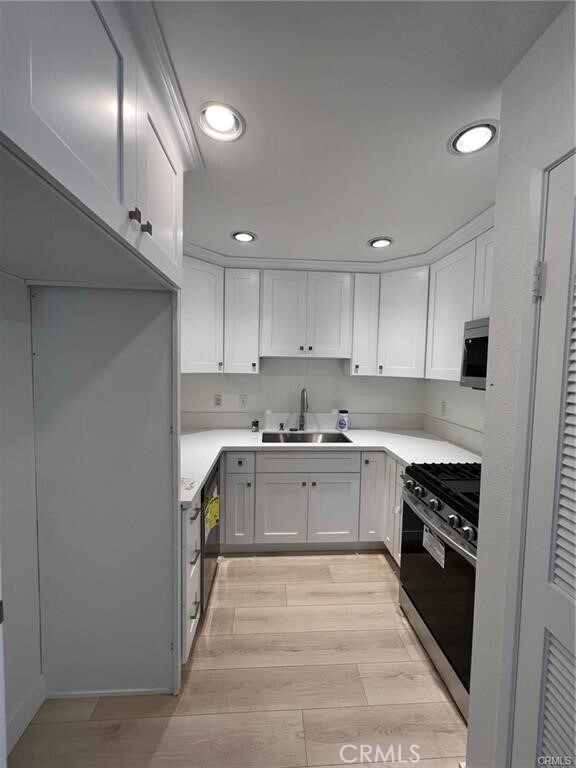 kitchen with sink, white cabinets, appliances with stainless steel finishes, and light hardwood / wood-style flooring