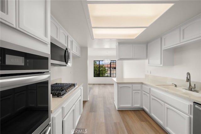 kitchen with kitchen peninsula, sink, white cabinets, light wood-type flooring, and stainless steel appliances