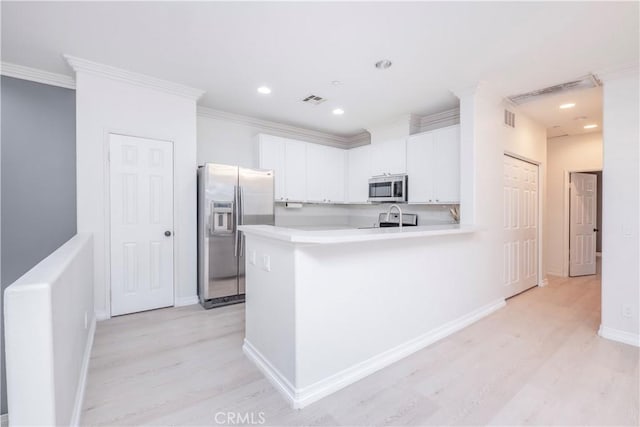 kitchen with crown molding, light hardwood / wood-style flooring, kitchen peninsula, stainless steel appliances, and white cabinets