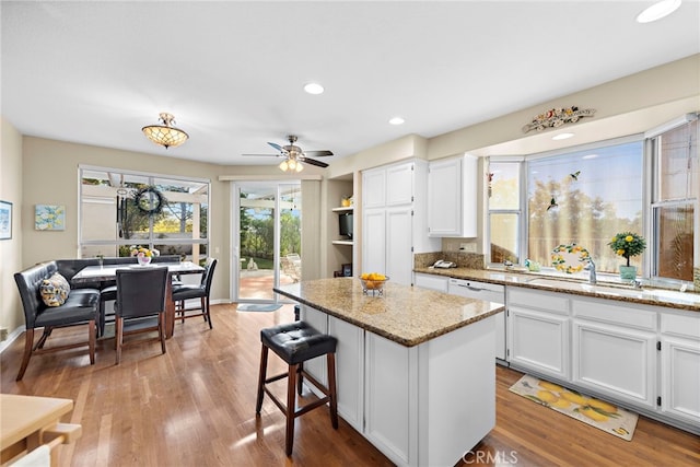 kitchen with ceiling fan, white cabinets, light stone countertops, a center island, and light hardwood / wood-style floors