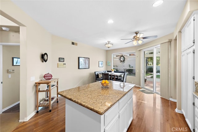 kitchen featuring hardwood / wood-style floors, light stone countertops, white cabinetry, a kitchen island, and ceiling fan