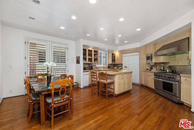 kitchen featuring built in appliances, a center island, wood-type flooring, a breakfast bar, and wall chimney exhaust hood