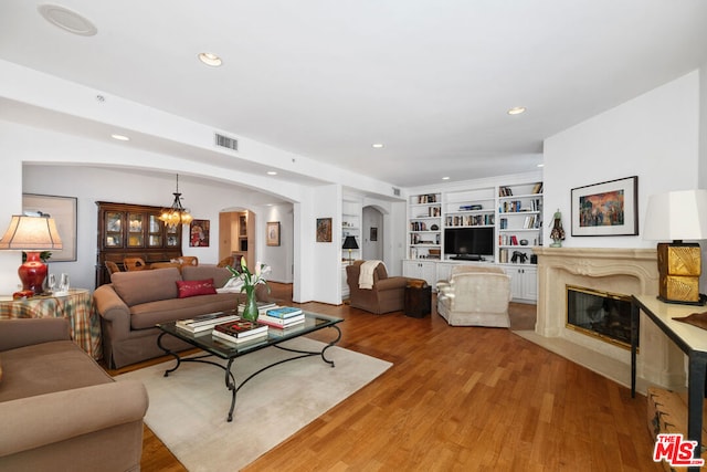 living room with light wood-type flooring, built in shelves, a notable chandelier, and a fireplace