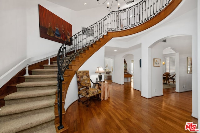 staircase featuring a notable chandelier, a towering ceiling, and wood-type flooring