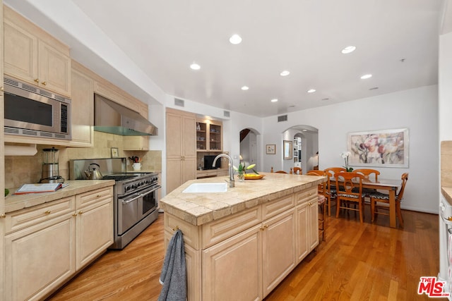 kitchen featuring wall chimney exhaust hood, a center island with sink, light hardwood / wood-style flooring, and appliances with stainless steel finishes