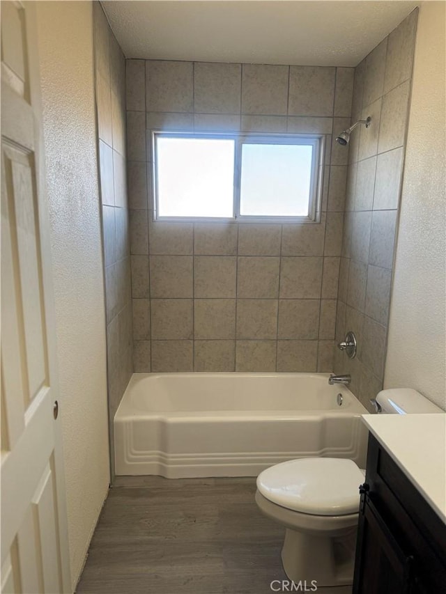 full bathroom with wood-type flooring, tiled shower / bath, vanity, and toilet