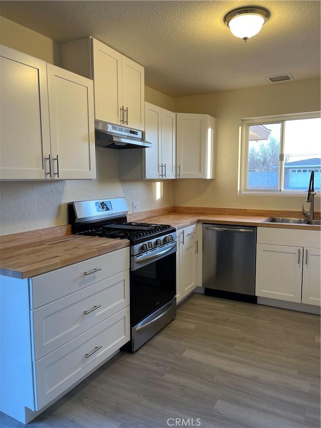 kitchen featuring butcher block countertops, white cabinetry, sink, stainless steel appliances, and a textured ceiling