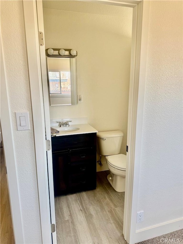 half bath with vanity, toilet, and wood finished floors