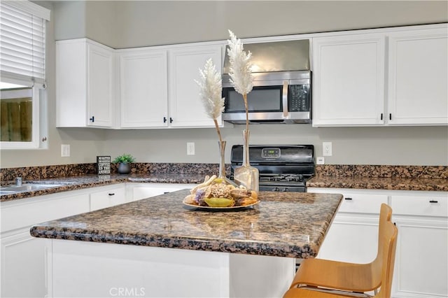 kitchen with a center island, black range oven, white cabinetry, dark stone countertops, and a breakfast bar