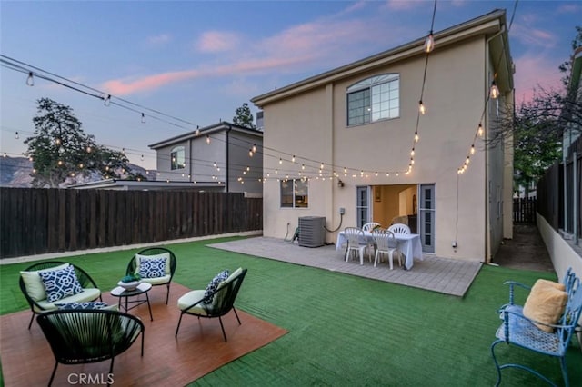 back house at dusk featuring central AC, a yard, and a patio