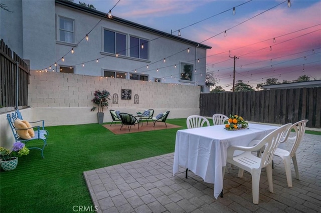 patio terrace at dusk featuring a lawn