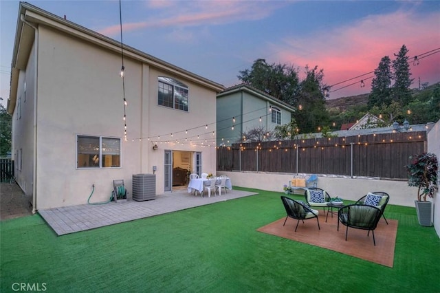 back house at dusk featuring central AC, a yard, and a patio