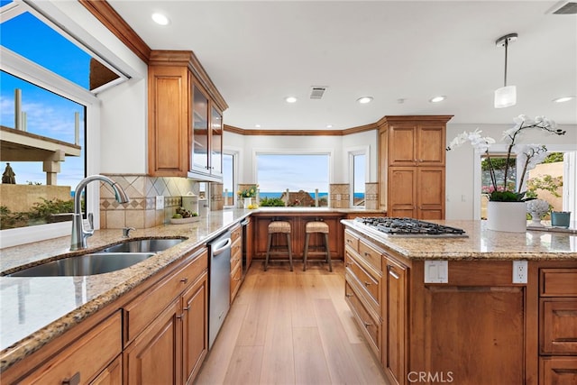 kitchen featuring appliances with stainless steel finishes, sink, hanging light fixtures, light stone countertops, and light hardwood / wood-style flooring