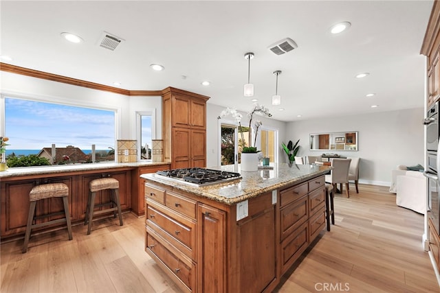 kitchen featuring a center island, hanging light fixtures, light wood-type flooring, appliances with stainless steel finishes, and light stone countertops