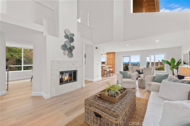 living room with light wood-type flooring, a high end fireplace, and a high ceiling