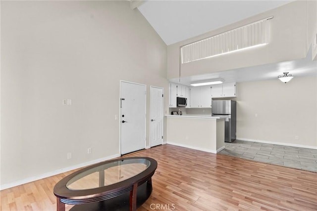 interior space featuring high vaulted ceiling, light wood-type flooring, and baseboards