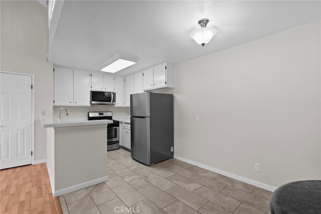 kitchen with baseboards, white cabinets, appliances with stainless steel finishes, a peninsula, and light countertops