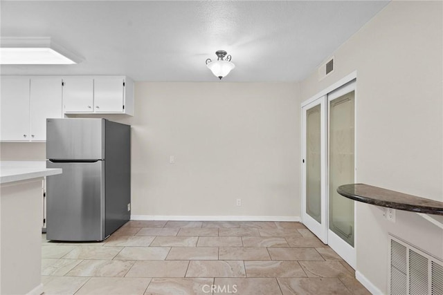 kitchen featuring baseboards, visible vents, white cabinetry, and freestanding refrigerator