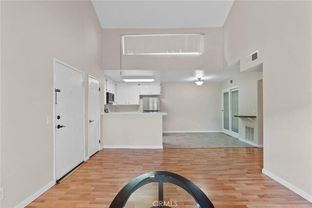 interior space featuring white cabinetry, stainless steel appliances, light hardwood / wood-style floors, and a high ceiling