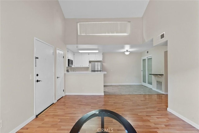 interior space with baseboards, a towering ceiling, visible vents, and light wood-style floors