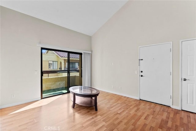 living area with light wood-type flooring, high vaulted ceiling, and baseboards