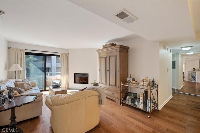 living room featuring a glass covered fireplace, visible vents, and wood finished floors