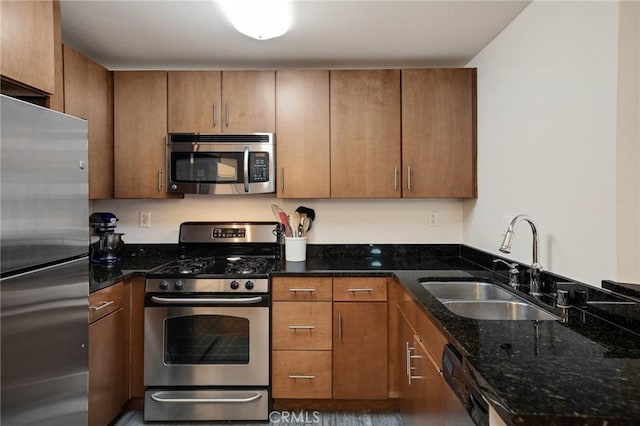 kitchen with brown cabinets, appliances with stainless steel finishes, dark stone counters, and a sink