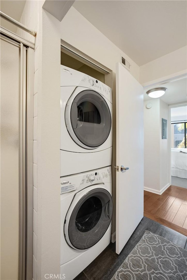 laundry area with visible vents, stacked washing maching and dryer, wood finished floors, electric panel, and baseboards