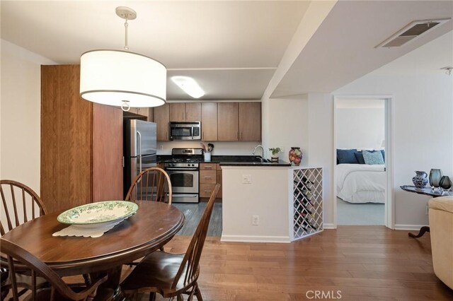 kitchen featuring a sink, wood finished floors, visible vents, appliances with stainless steel finishes, and dark countertops