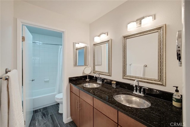 full bath with double vanity, a sink, toilet, and wood finished floors