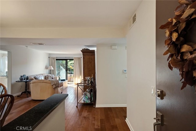 hall featuring dark wood-style floors, visible vents, and baseboards