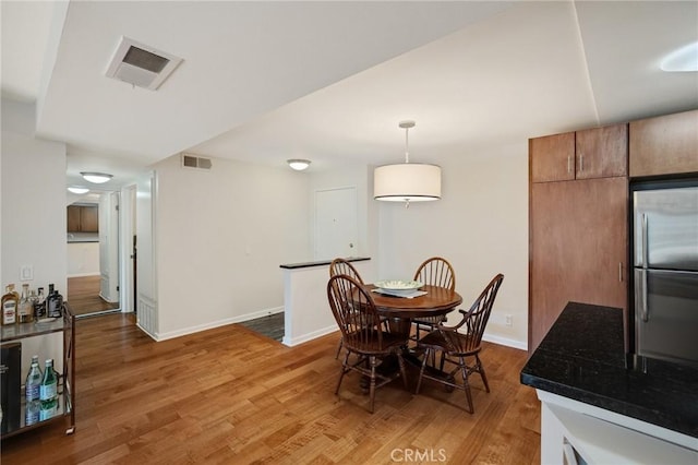 dining room with light wood-type flooring, visible vents, and baseboards