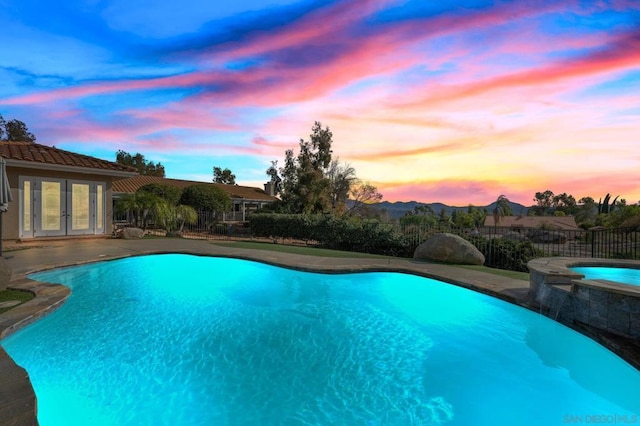 pool at dusk featuring a patio, french doors, and an in ground hot tub