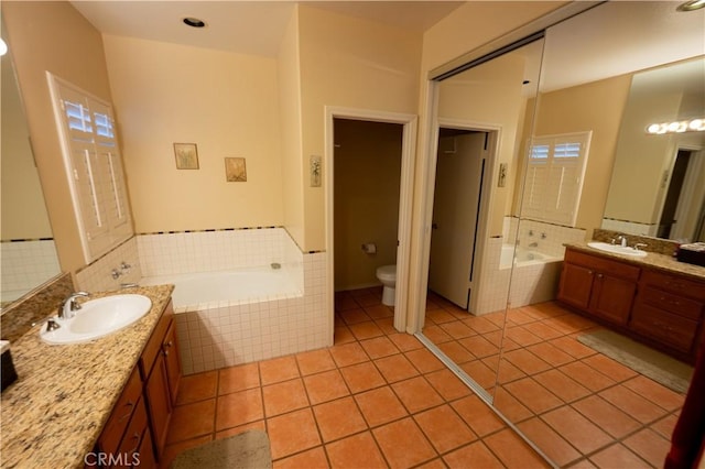 bathroom featuring tiled tub, vanity, tile patterned floors, and toilet