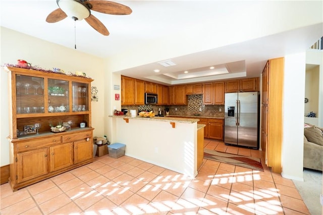 kitchen featuring light tile patterned flooring, appliances with stainless steel finishes, a tray ceiling, backsplash, and kitchen peninsula