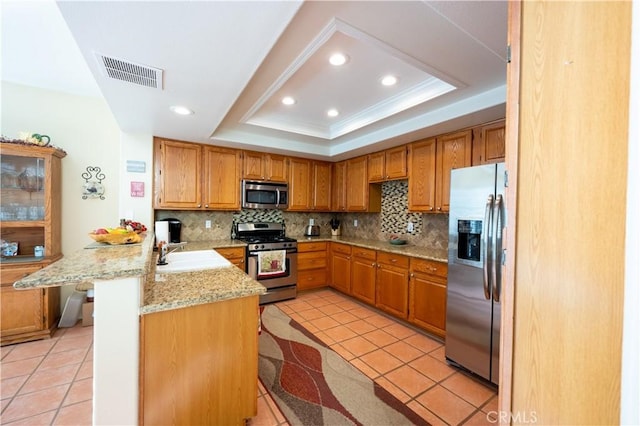 kitchen featuring sink, a breakfast bar area, appliances with stainless steel finishes, a raised ceiling, and kitchen peninsula