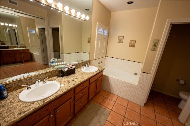 bathroom with tile patterned flooring, vanity, tiled tub, and toilet