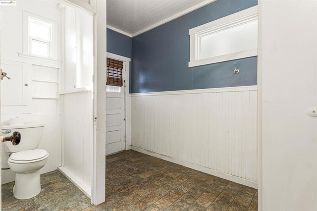 bathroom with toilet, crown molding, and wooden walls