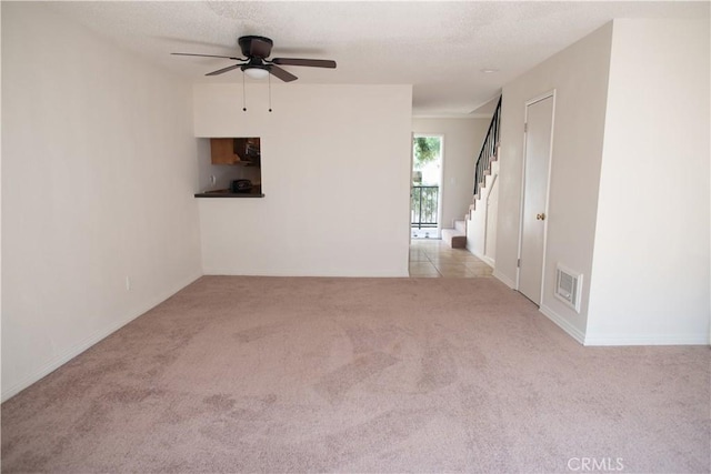 carpeted spare room with a ceiling fan, visible vents, stairway, and a textured ceiling