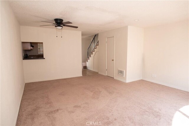 carpeted empty room with ceiling fan, stairs, visible vents, and a textured ceiling