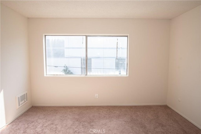 spare room with a healthy amount of sunlight, baseboards, light carpet, and visible vents