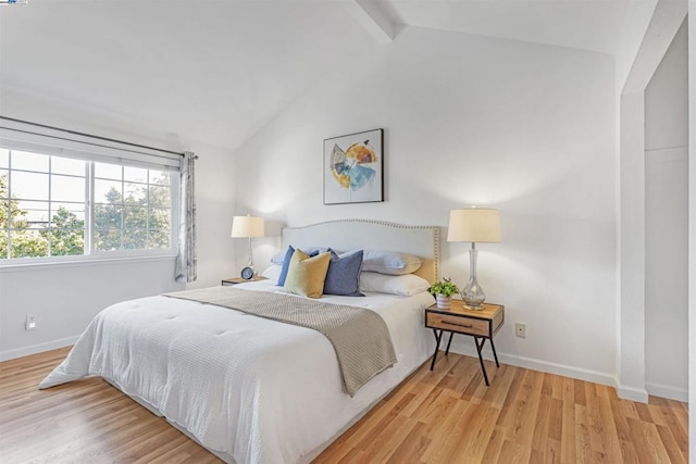 bedroom with light hardwood / wood-style floors and vaulted ceiling with beams