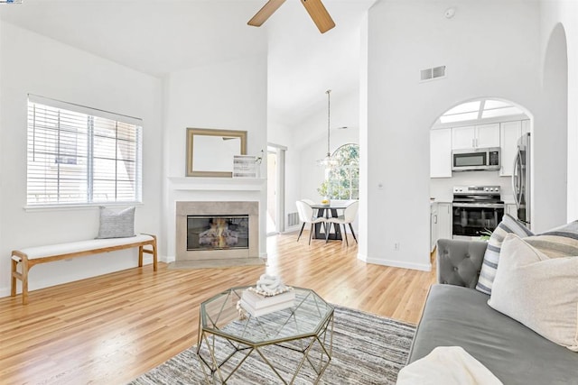 living room with light hardwood / wood-style floors, ceiling fan, and a towering ceiling