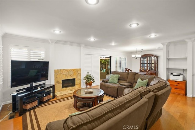 living room with a notable chandelier, a stone fireplace, crown molding, and light hardwood / wood-style floors