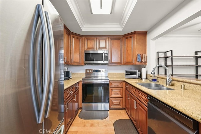 kitchen with sink, light wood-type flooring, stainless steel appliances, light stone counters, and a tray ceiling