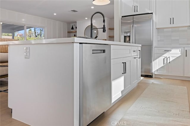 kitchen with appliances with stainless steel finishes, white cabinetry, sink, backsplash, and a center island with sink