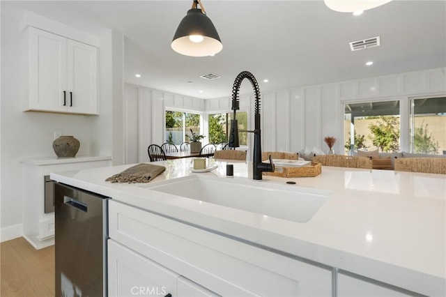 kitchen featuring decorative light fixtures, white cabinetry, dishwasher, sink, and light hardwood / wood-style floors