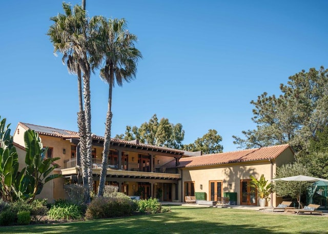 rear view of house with a patio, a yard, french doors, and a balcony